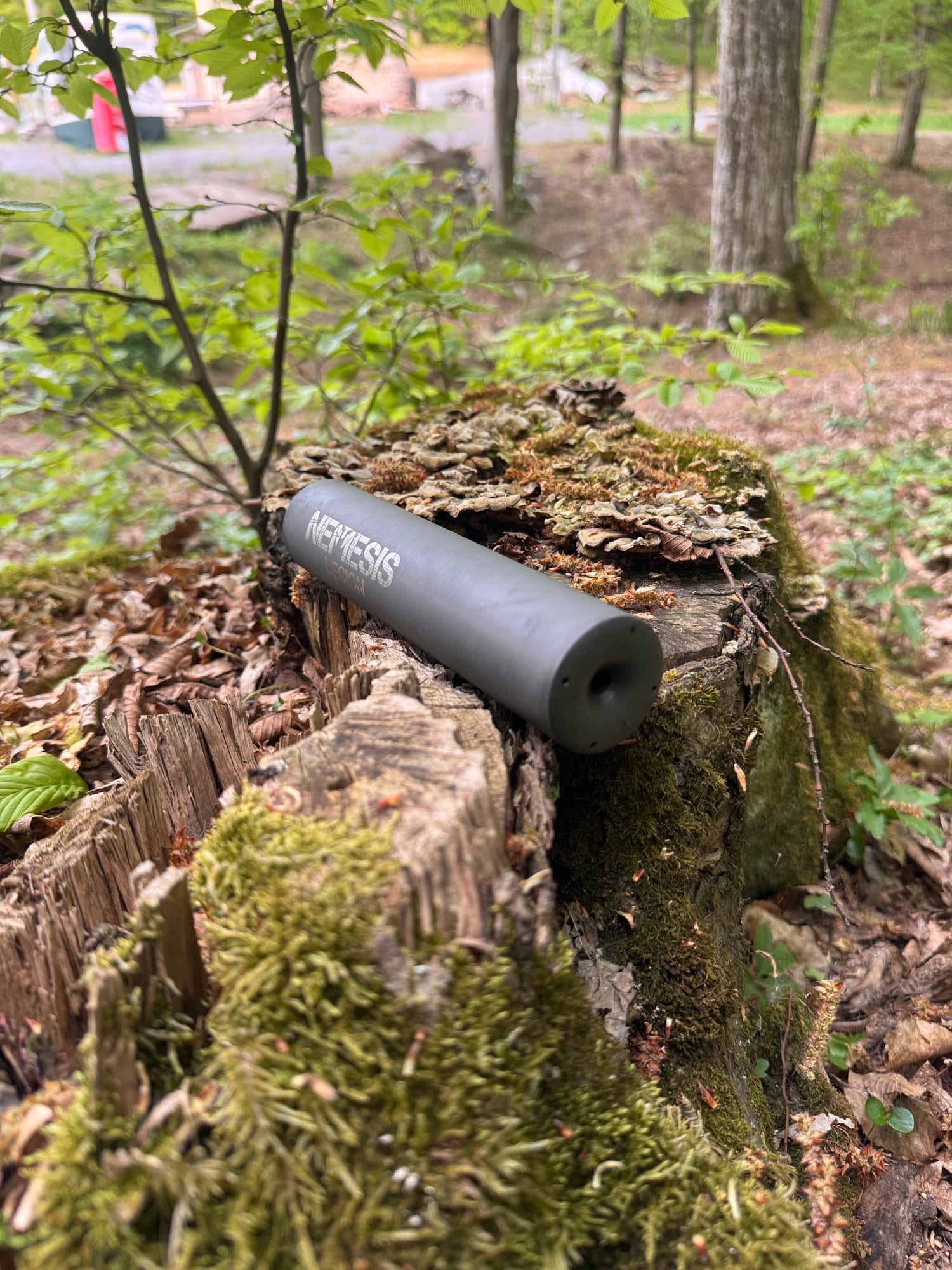 Саундмодератор NEMESIS CORE 7.62 лежить на пні в лісі - вид збоку з торцем і корпусом під кутом