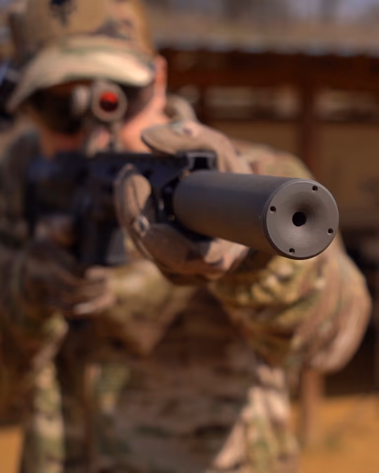 Саундмодератор NEMESIS CORE 9mm накручений на AR-9, вид на торець із вихідним каналом і газовими отворами - солдат у multicam цілиться