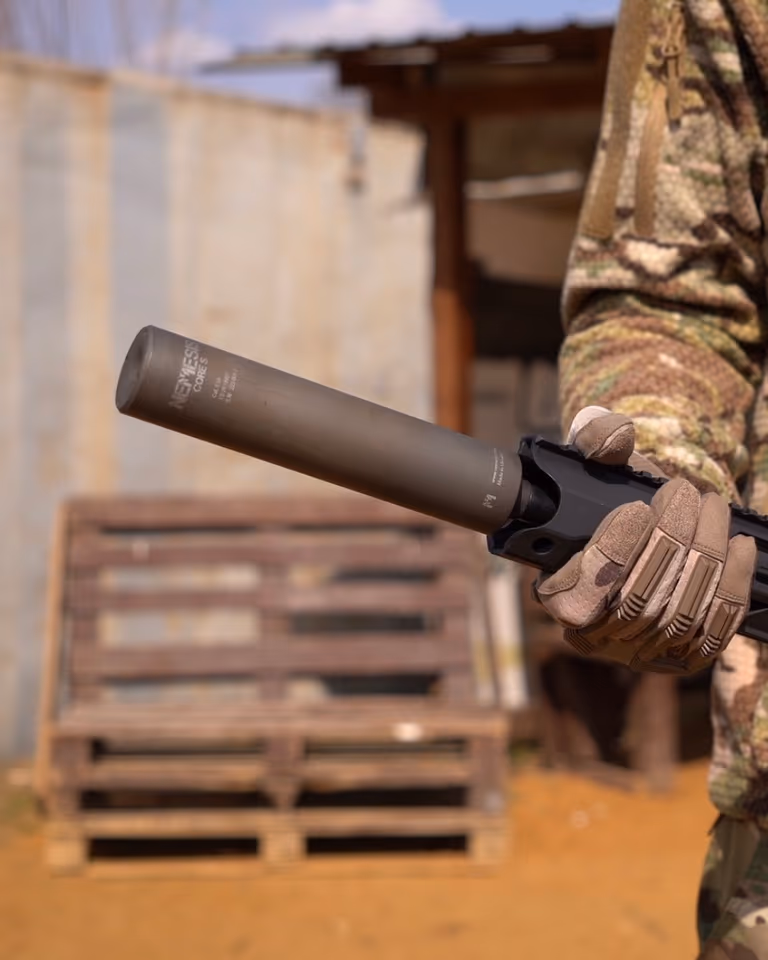 Глушник NEMESIS CORE 9mm з гравіюванням у тактичній рукавиці на тлі піддонів, вид збоку - накручений на зброю