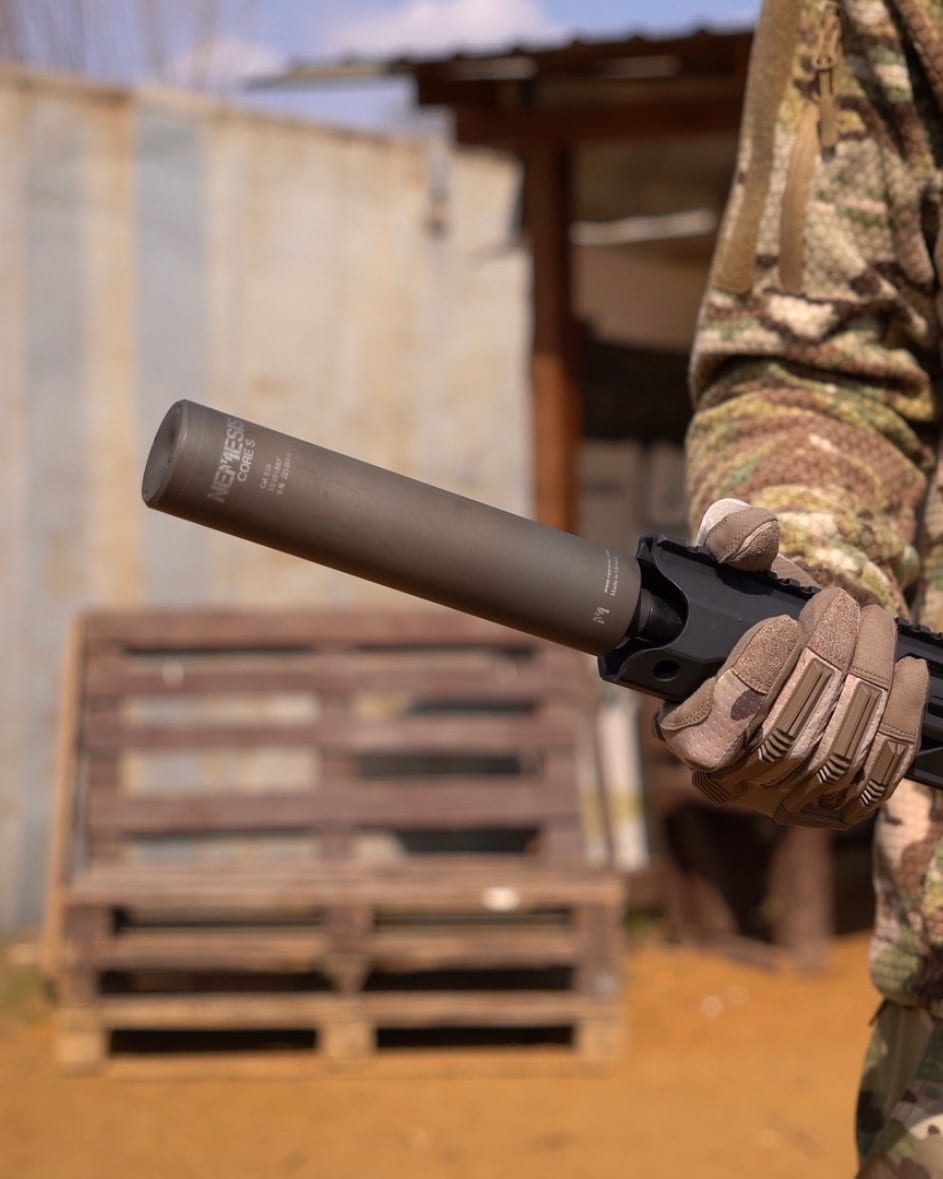 Глушник NEMESIS CORE 9mm з гравіюванням у тактичній рукавиці на тлі піддонів, вид збоку - накручений на зброю