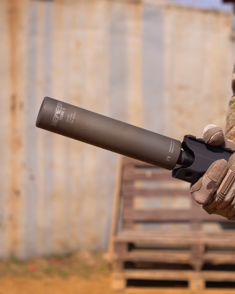 Глушник NEMESIS CORE 9mm накручений на зброю в тактичній рукавиці на тлі контейнера - вид збоку з гравіюванням