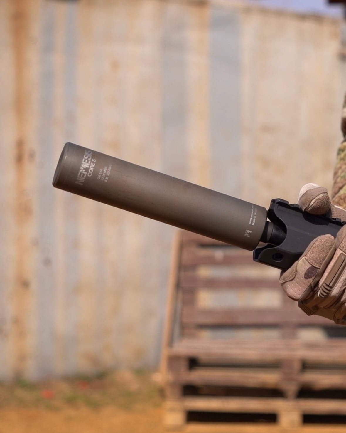 Глушник NEMESIS CORE 9mm накручений на зброю в тактичній рукавиці на тлі контейнера - вид збоку з гравіюванням
