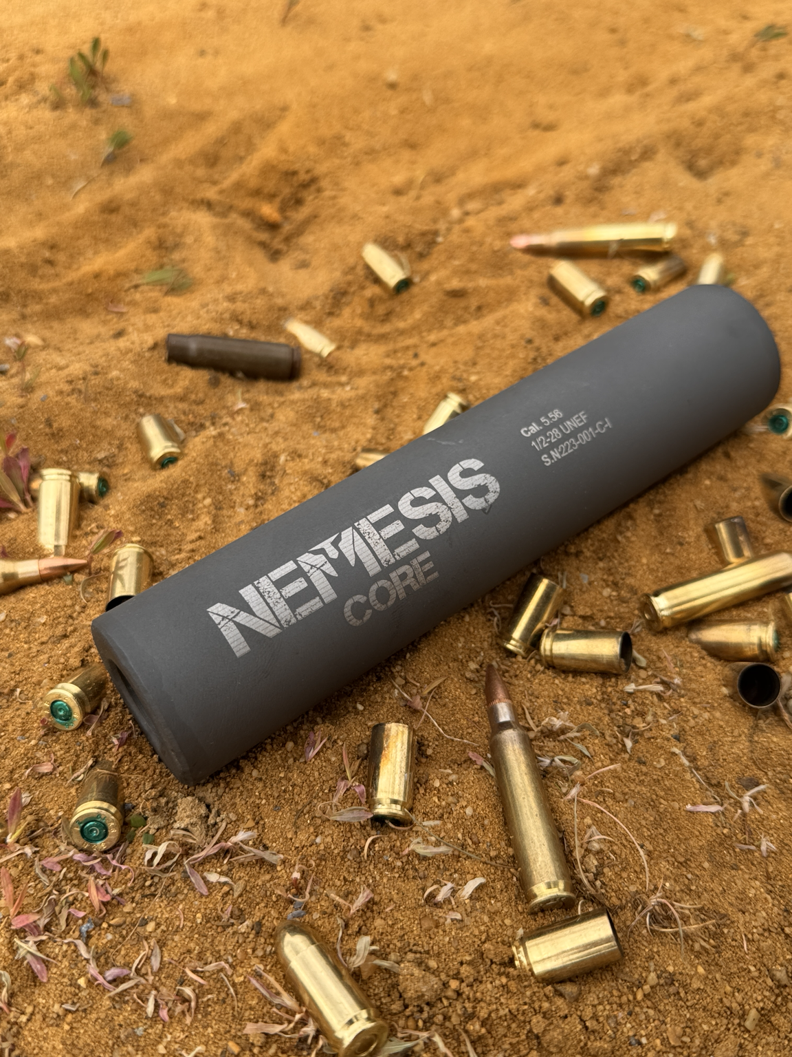 Саундмодератор NEMESIS CORE 5.56 на стрільбищі серед гільз, видно гравіювання NEMESIS CORE і маркування Cal. 5.56 1/2-28