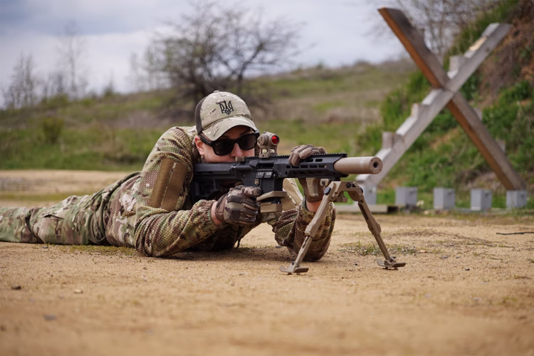 Стрілець лежить і цілиться з AR-15 з глушником NEMESIS CORE 5.56, вид ззаду на стрільця і ціль