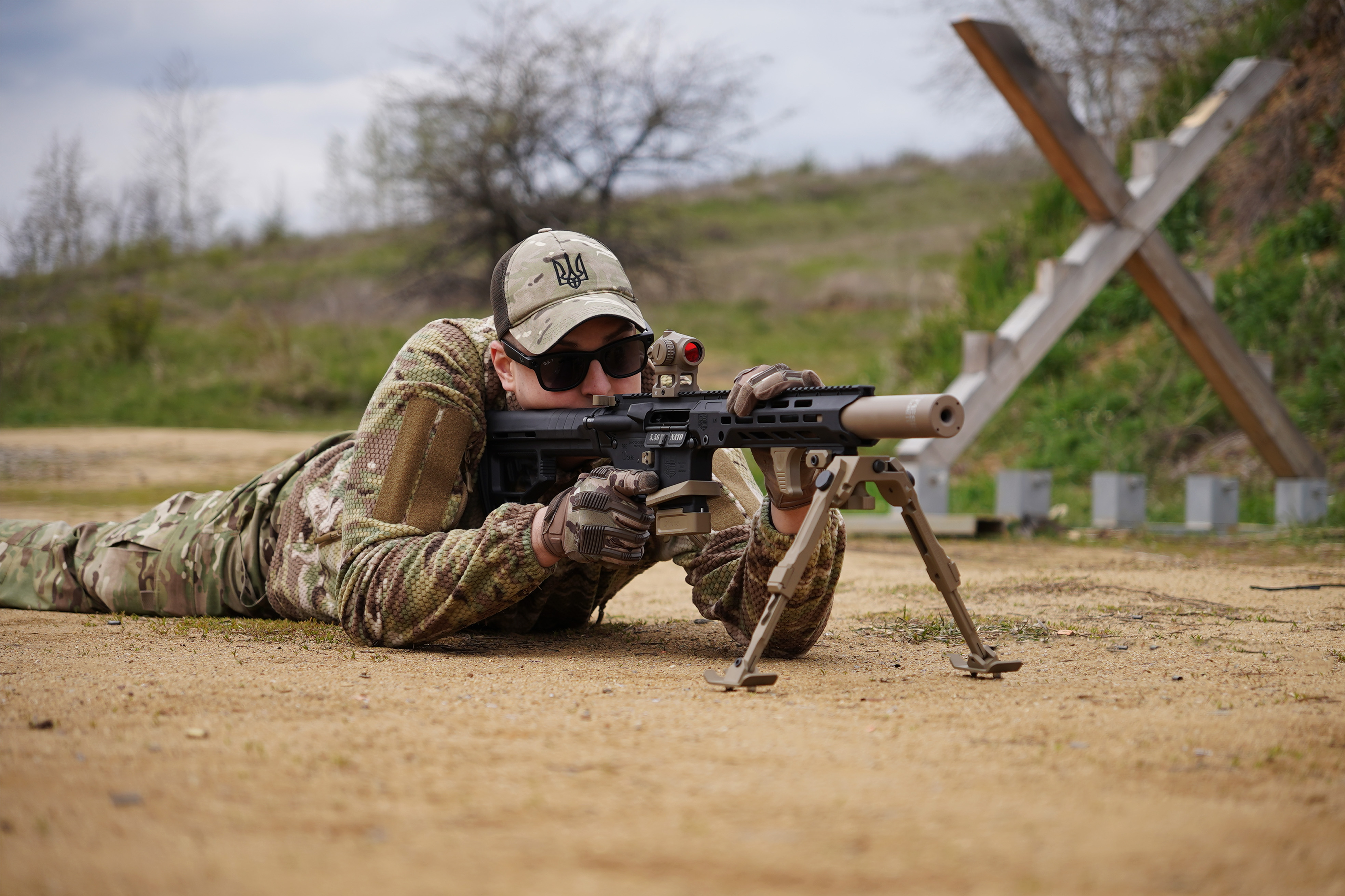Стрілець лежить і цілиться з AR-15 з глушником NEMESIS CORE 5.56, вид ззаду на стрільця і ціль
