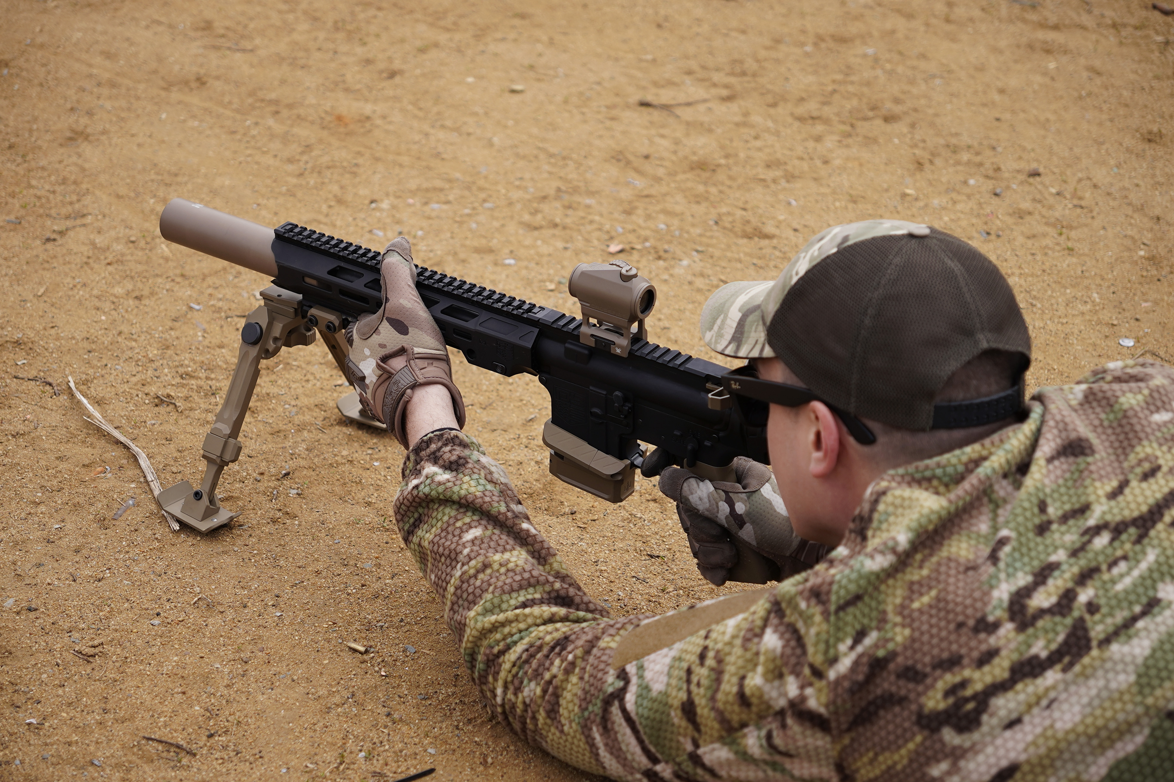 Стрілець у мультикамі цілиться з AR-15 5.56 з глушником NEMESIS CORE на сошках, вид збоку крупним планом