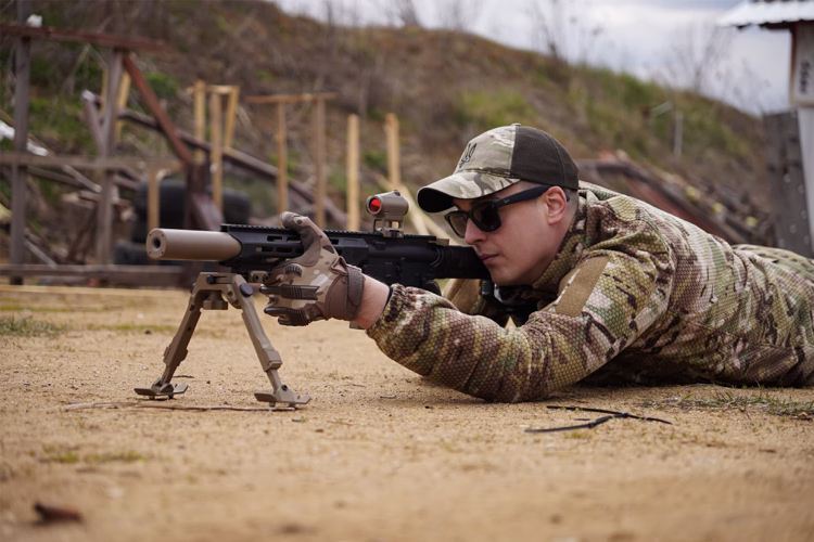AR-15 5.56 NATO на сошках на піску - глушник NEMESIS CORE накручений на ствол, вид збоку, коліматорний приціл