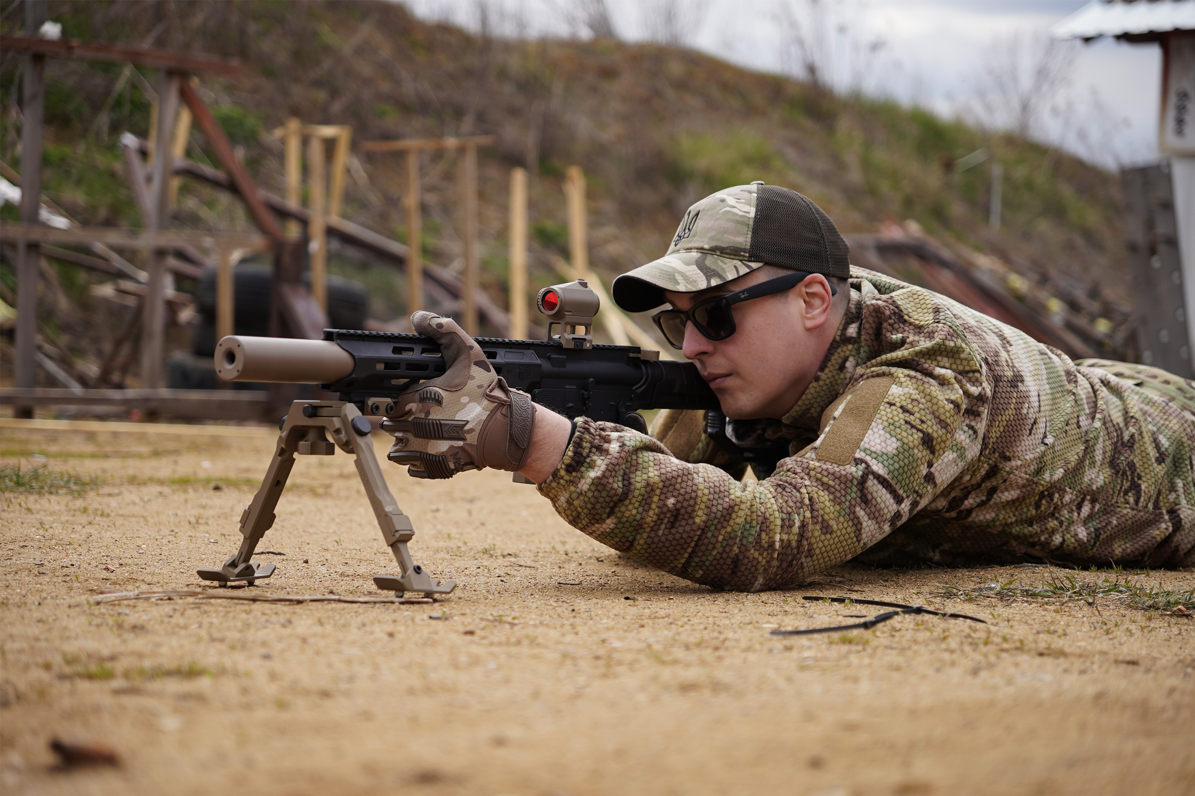 AR-15 5.56 NATO на сошках на піску - глушник NEMESIS CORE накручений на ствол, вид збоку, коліматорний приціл