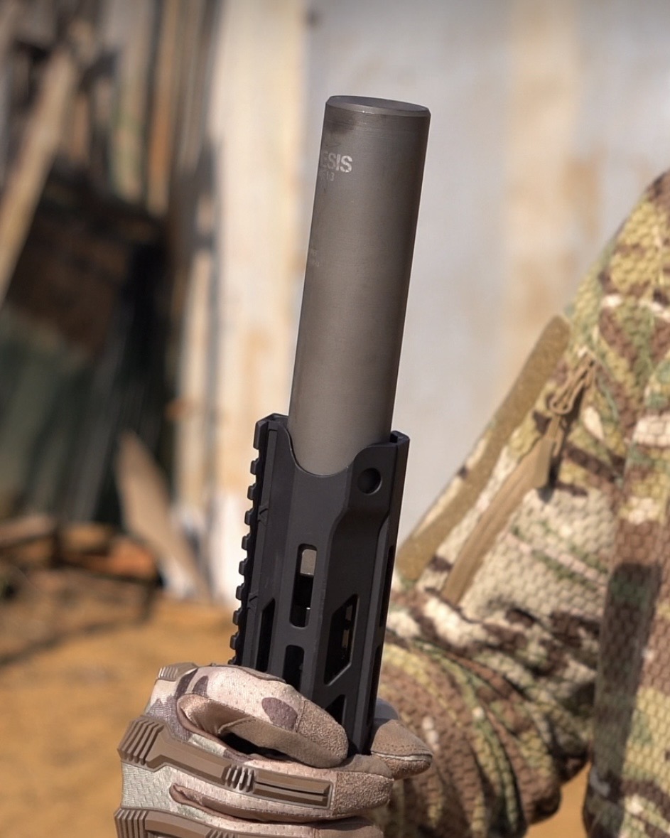 Глушник NEMESIS CORE Internal 5.56 у тактичній рукавиці на тлі цивільної будівлі, вид збоку із написом NEMESIS