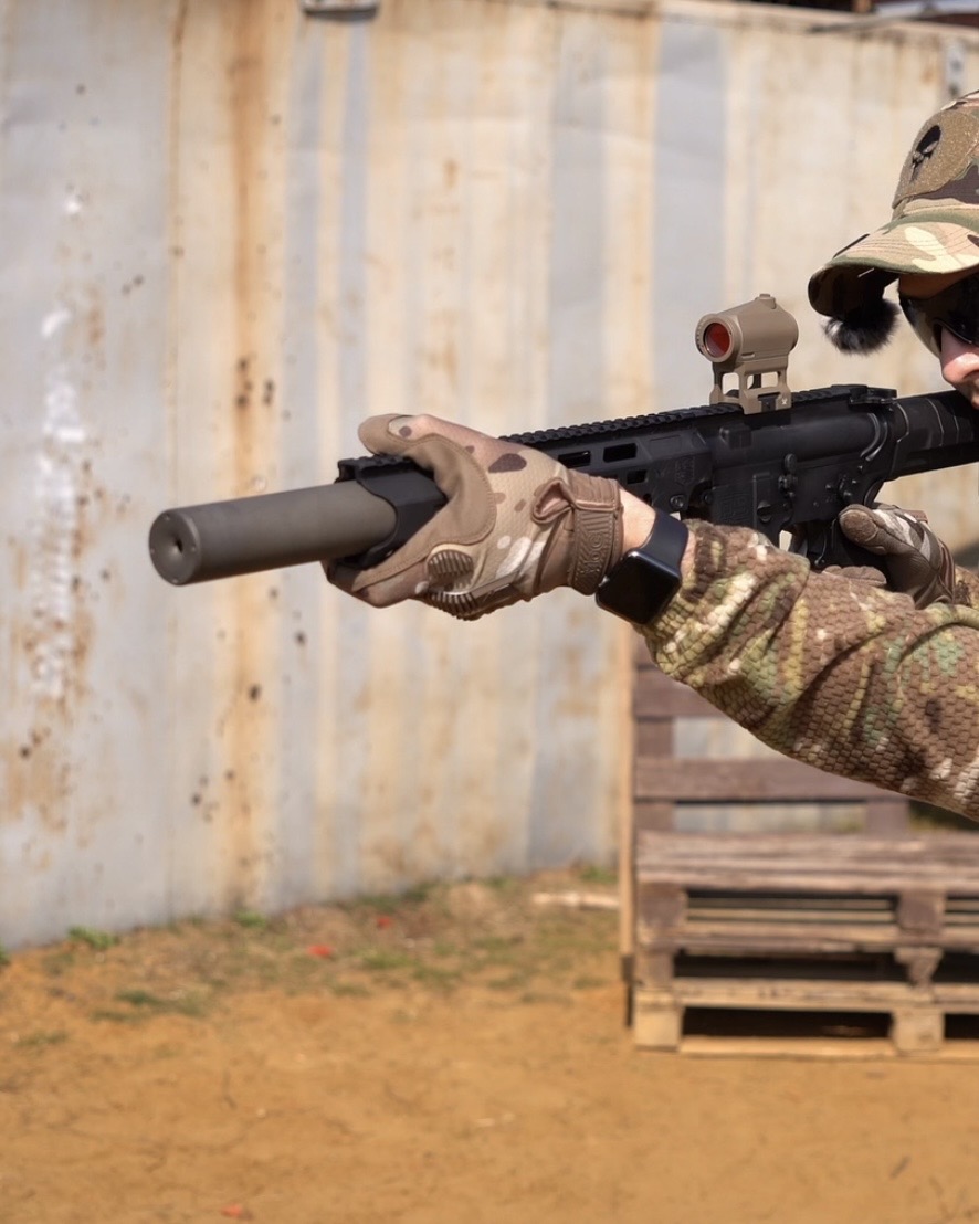 Саундмодератор NEMESIS CORE 5.56 накручений на AR-15, стрілець в обмундируванні цілиться з ергономічним цівьом