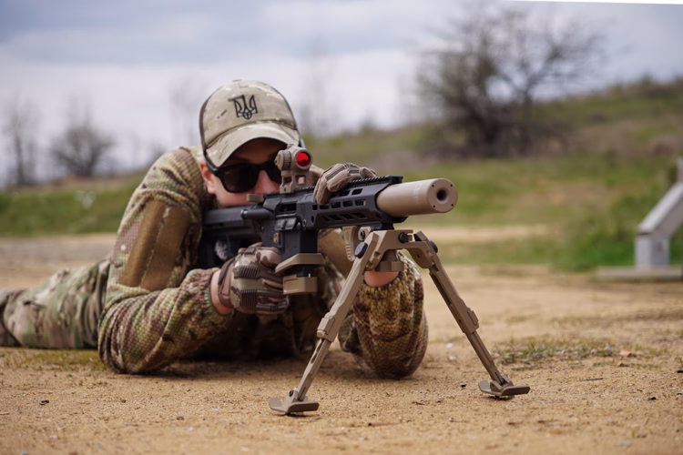 Стрілець лежить із AR-15 калібру 5.56 NATO на сошках, саундмодератор NEMESIS CORE накручений на ствол - вид збоку