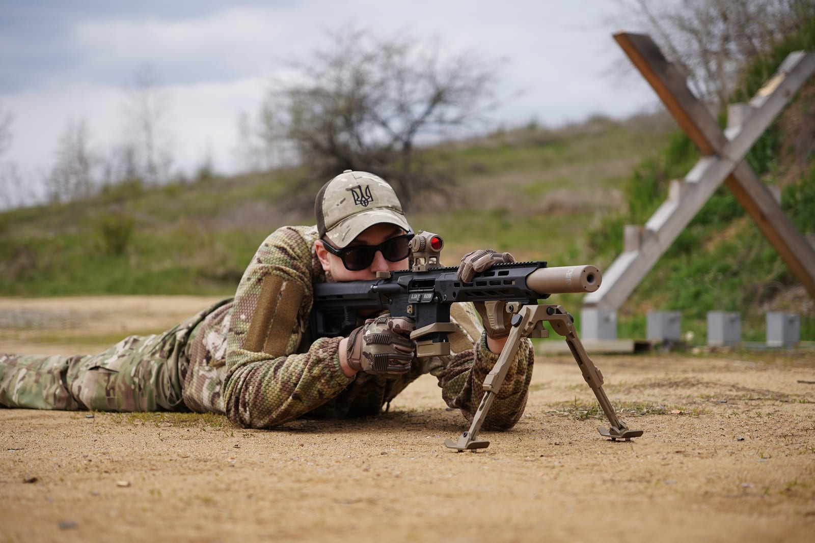 Стрілець із NEMESIS CORE 9mm на PCC прицілюється лежачи зі сошками, вид збоку на полігоні