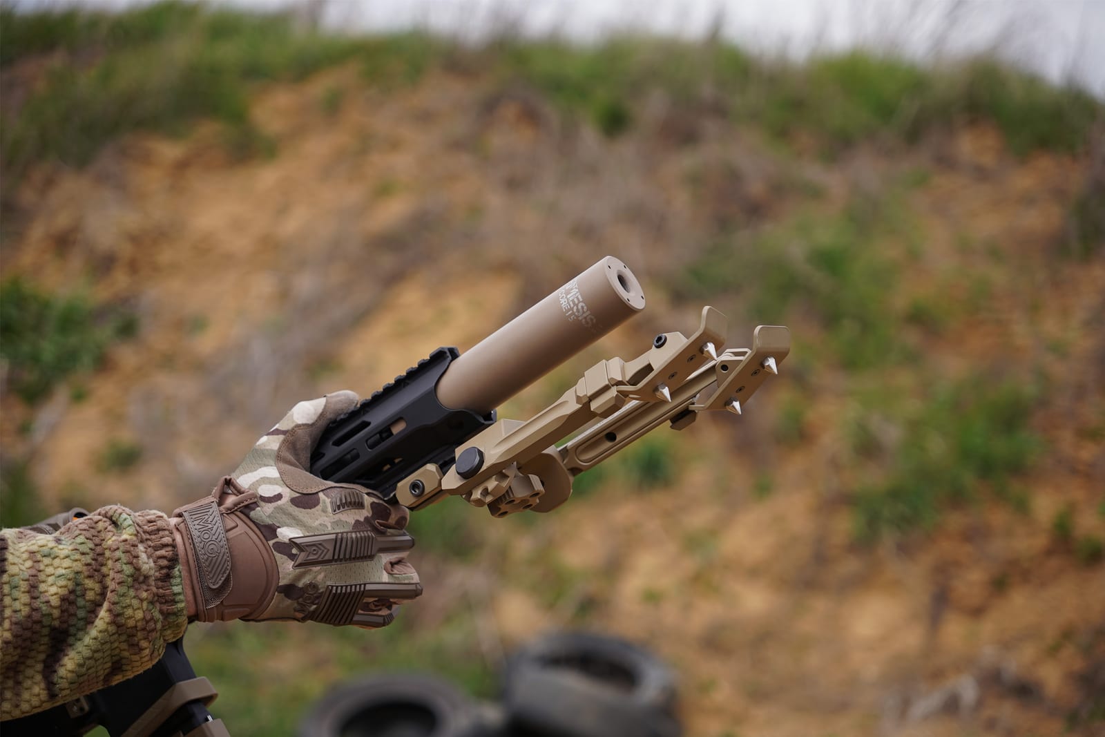 Глушник NEMESIS CORE Internal 9mm на PCC у тактичній рукавиці, вид збоку крупним планом на тлі схилу