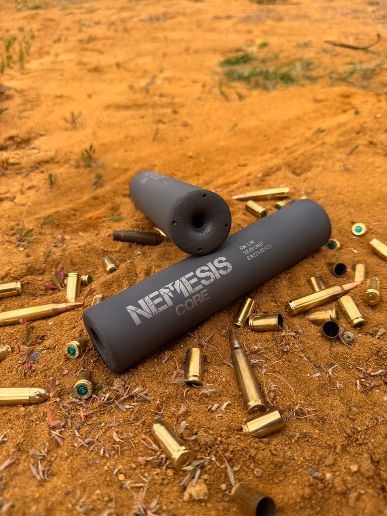 Розібраний саундмодератор NEMESIS CORE 9mm: корпус і знятий торцевий елемент лежать на піску серед гільз