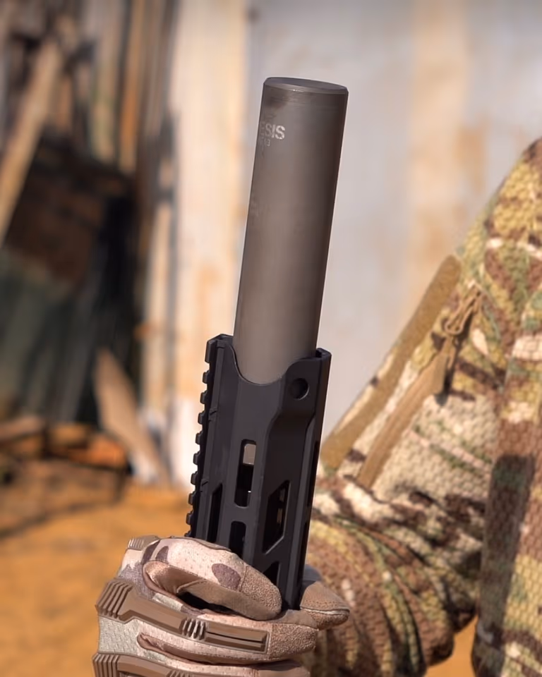 Глушник NEMESIS CORE Internal 9mm у тактичній рукавиці вертикально на тлі стіни, видно гравіювання NEMESIS Core i3
